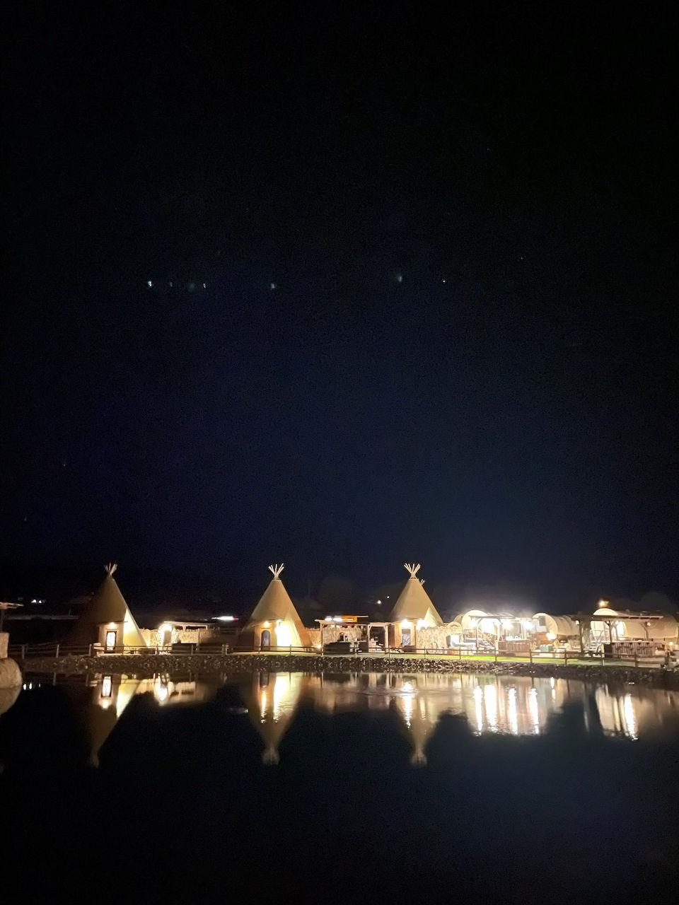 A cozy tepee illuminated by the light of a campfire at night, with the starry sky in the background.