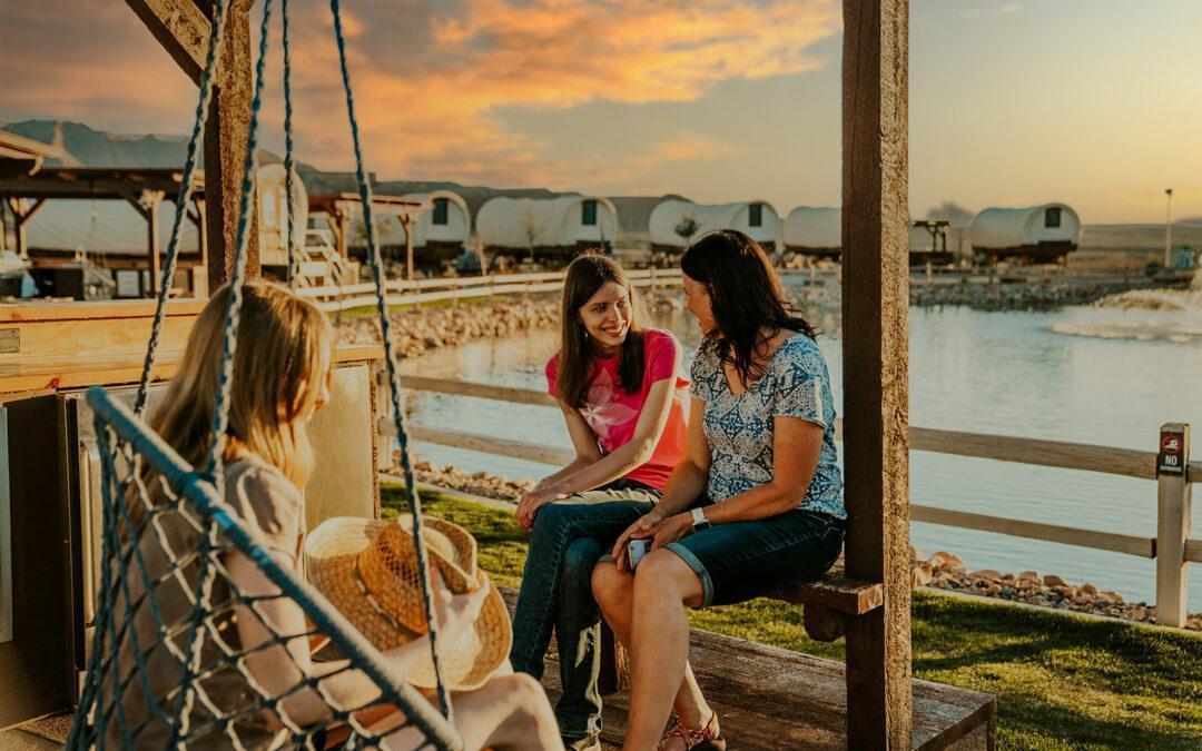 Family enjoying a relaxing outdoor moment at a glamping site with a scenic sunset view.