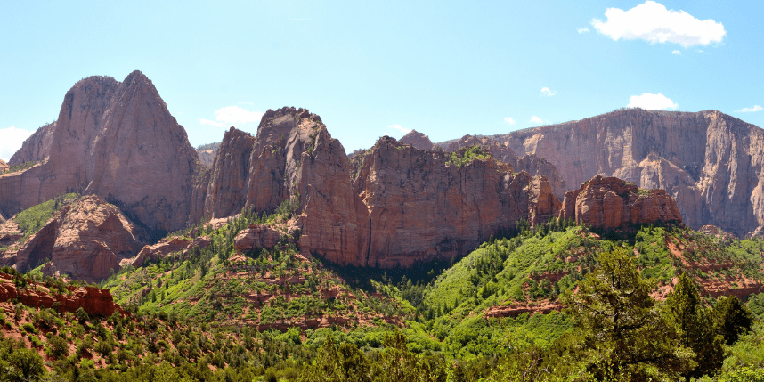 Scenic view of trails near St. George with towering red cliffs and green foliage under a bright blue sky.