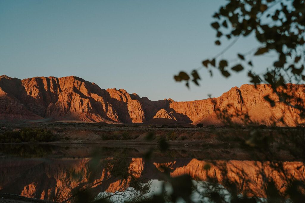 Beautiful outdoor scenery of Zion's cliffs reflecting on a calm lake at sunset, illustrating the natural allure of outdoor glamping vs indoor glamping.