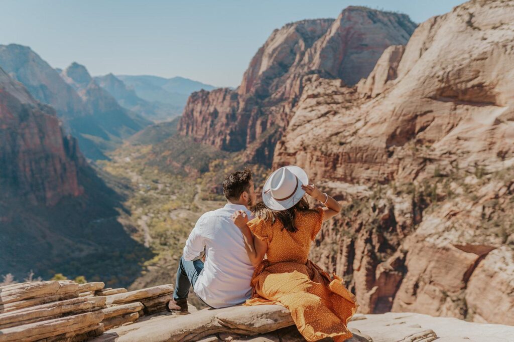 Couple sitting on the edge of cliff enjoying the view of Zion National Park