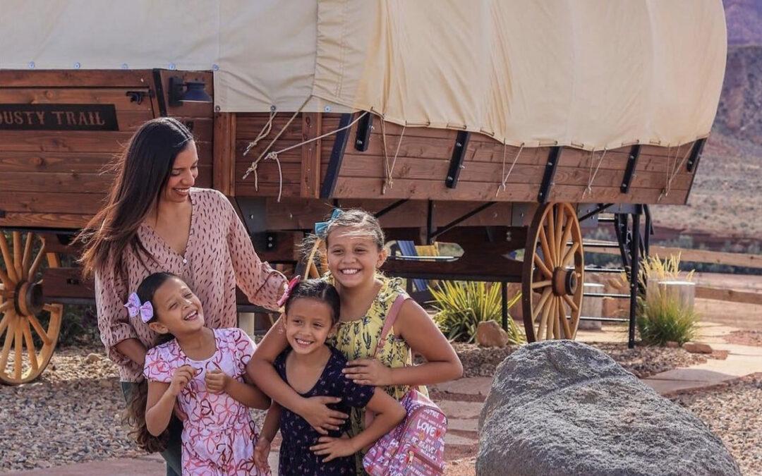 mother and three daughters smiling with a covered wagon behind