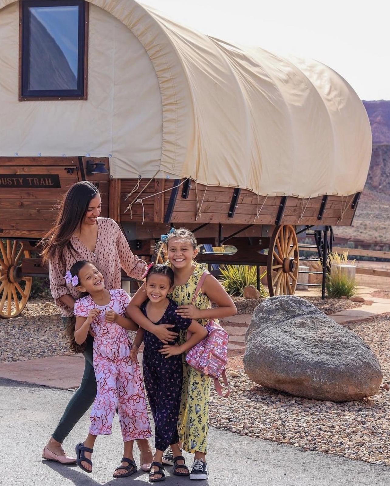 mother and three daughters smiling with a covered wagon behind